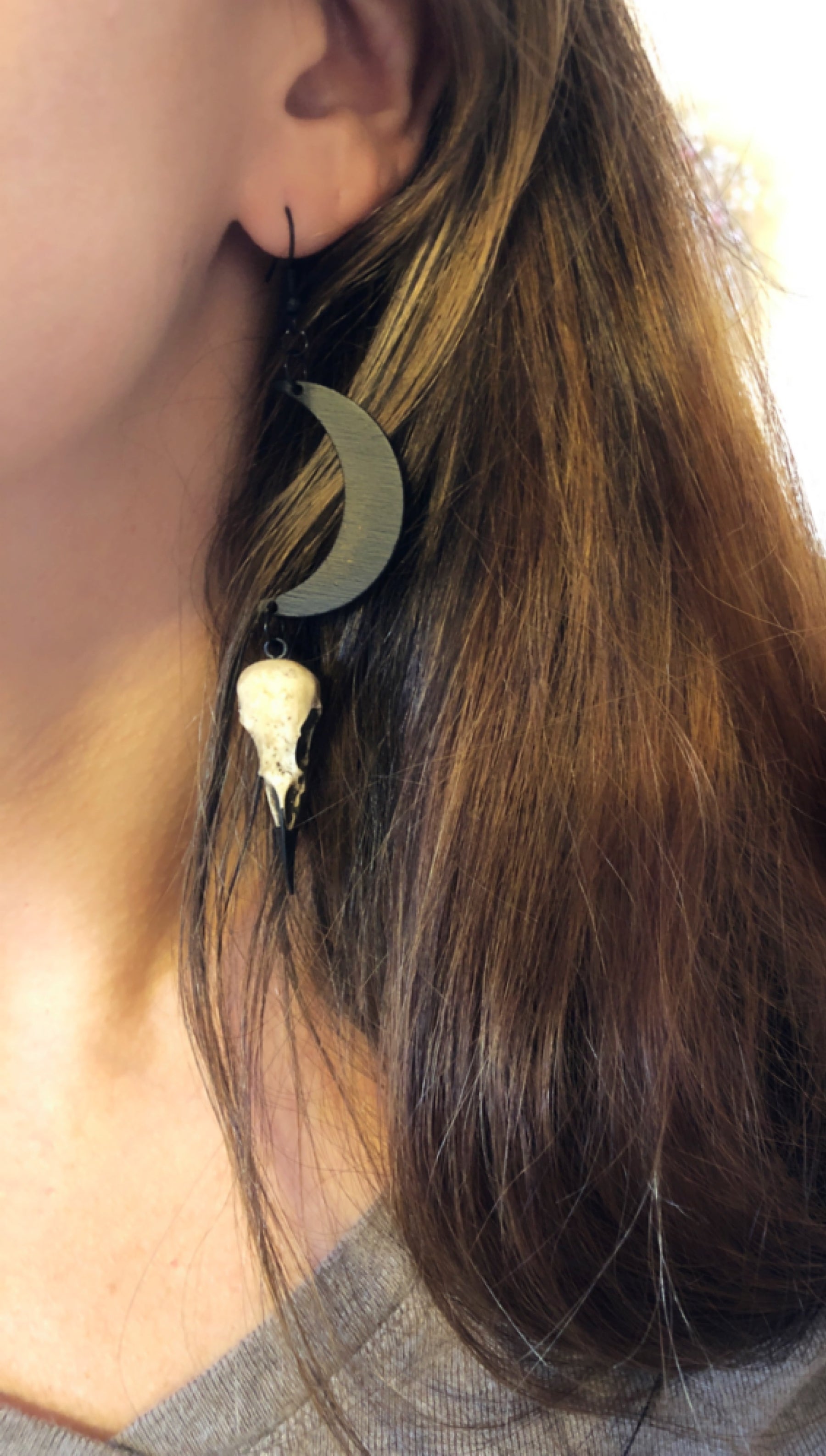 Witchy woman wearing gift idea Dangle earlobe raven goth skull charm earrings with crescent moons and resin bird skulls.