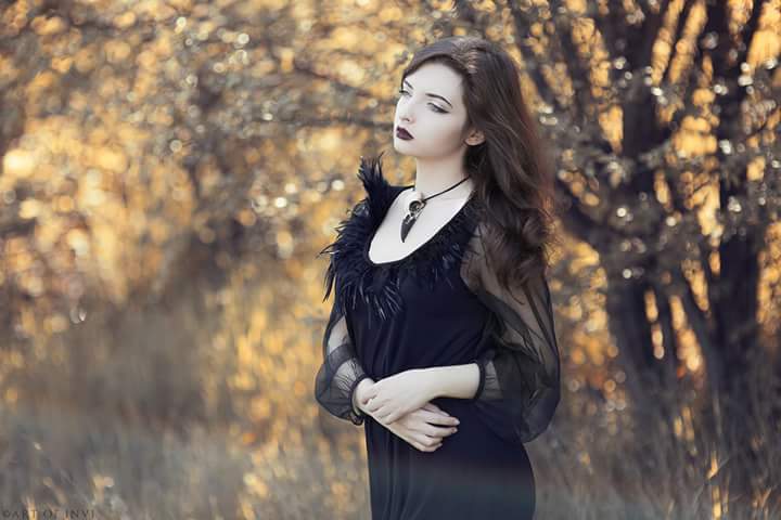 Raven queen wearing large resin raven skull pendant bird skull bone jewelry and black feather top.