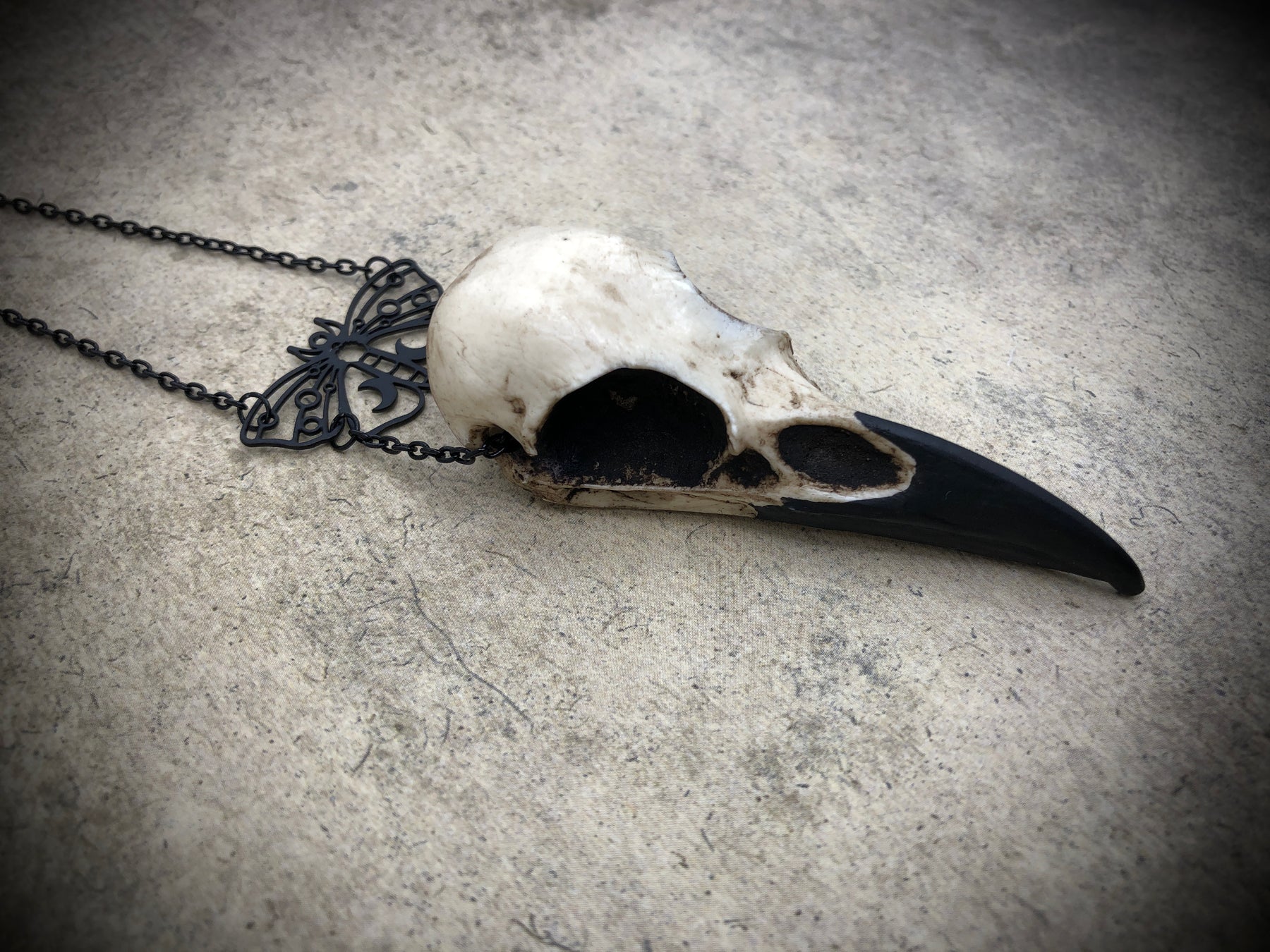 Side view of Gothic black death moth luna butterfly charm pendant and bone jewelry mini raven skull dangle pendant.