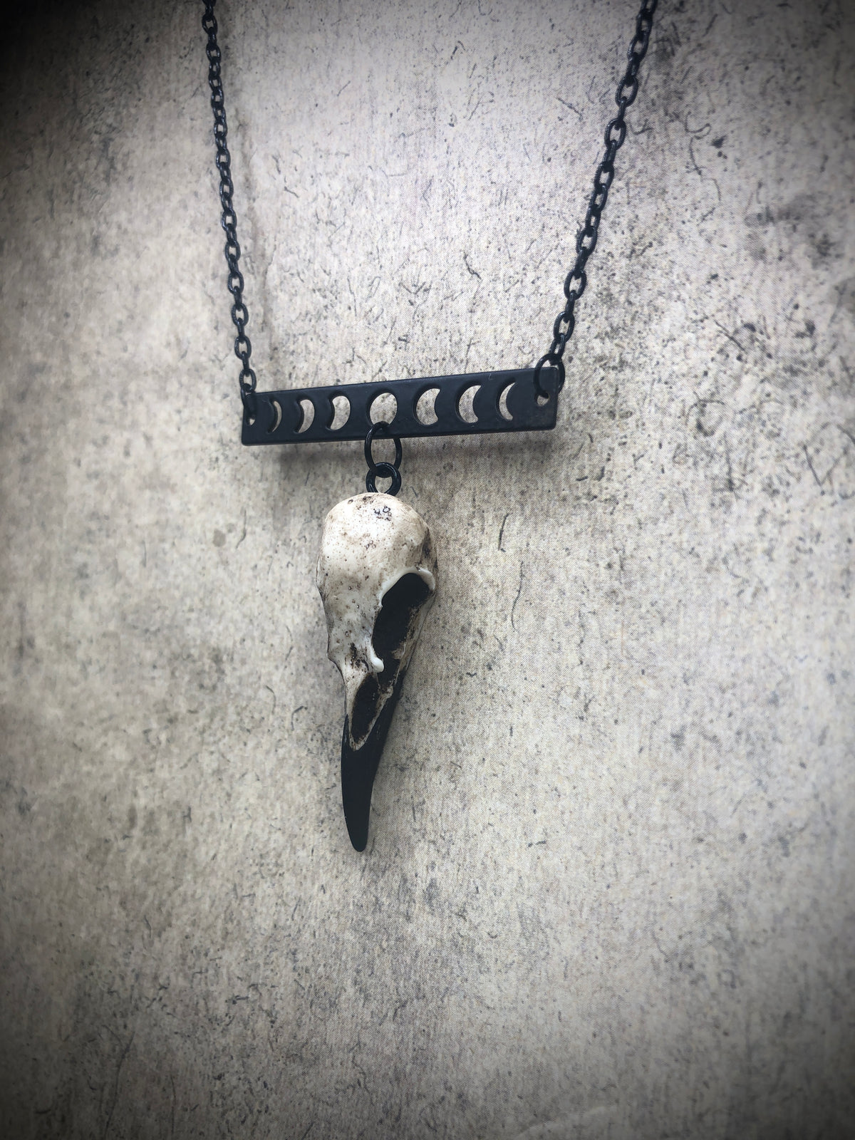Side view of lunar moon phase horizontal bar charm pendant and bone jewelry mini resin raven skull dangle pendant.