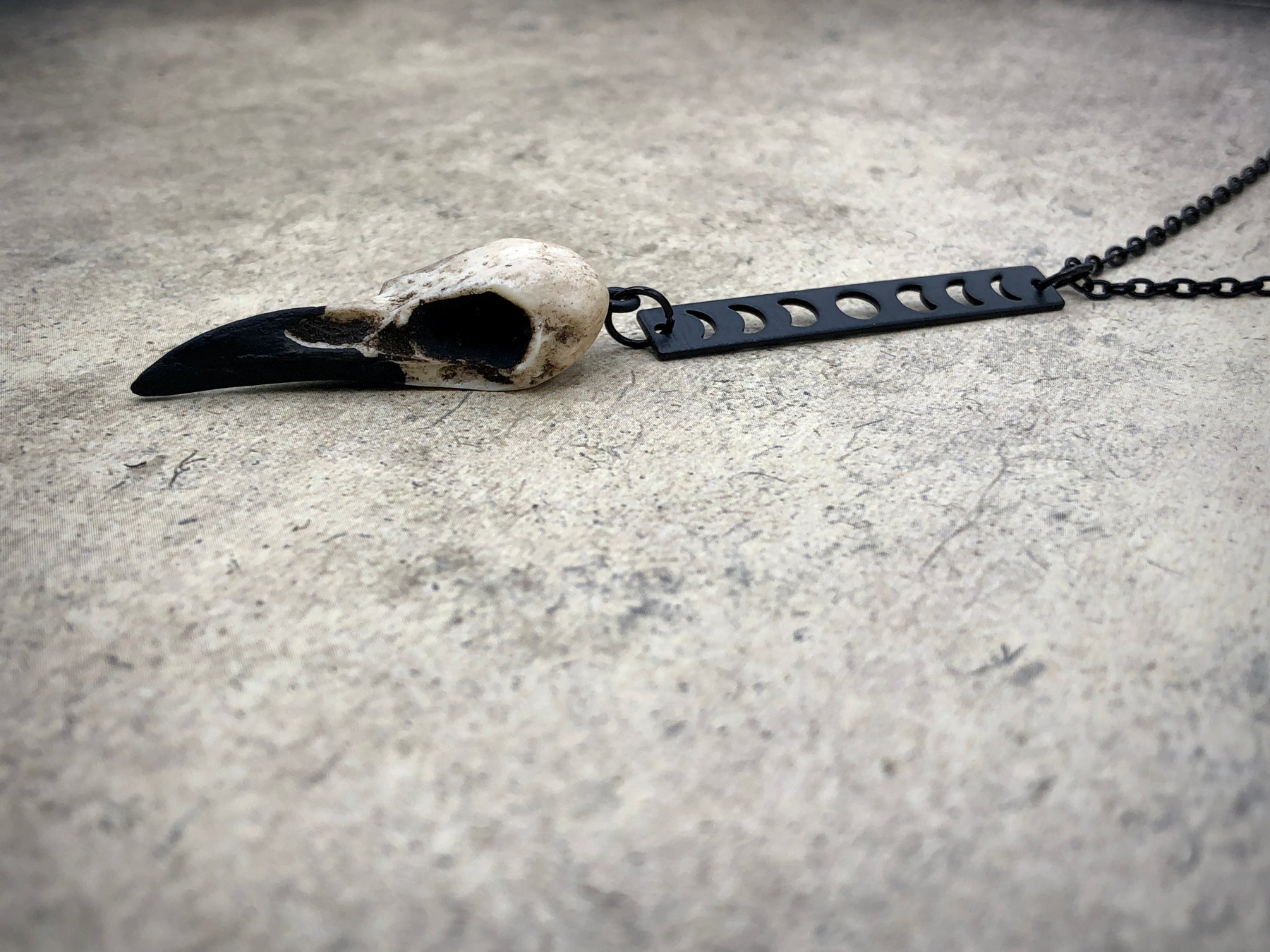 Close up view of Moon phase vertical bar charm pendant and bone jewelry mini resin raven bird skull dangle pendant.