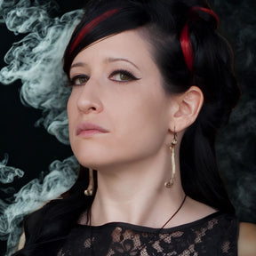 Alt model wearing resin femur bone dangle earrings that are handmade by Raven Ranch Studio, an expert resin skull artist.