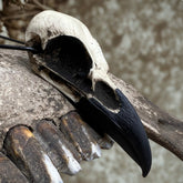A life size resin raven skull necklace handmade by a skull jewelry artist and worn by gothic alt model. The style of the necklace is alternative and witchy for gothic fashion or Halloween. The bone jewelry pendant is brown with a black beak and looks like a real animal skull.