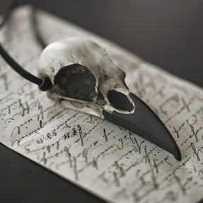 A life size resin raven skull necklace handmade by a skull jewelry artist and worn by gothic alt model. The style of the necklace is alternative and witchy for gothic fashion or Halloween. The bone jewelry pendant is brown with a black beak and looks like a real animal skull.