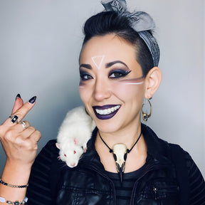 A life size resin raven skull necklace handmade by a skull jewelry artist and worn by gothic alt model. The style of the necklace is alternative and witchy for gothic fashion or Halloween. The bone jewelry pendant is brown with a black beak and looks like a real animal skull.