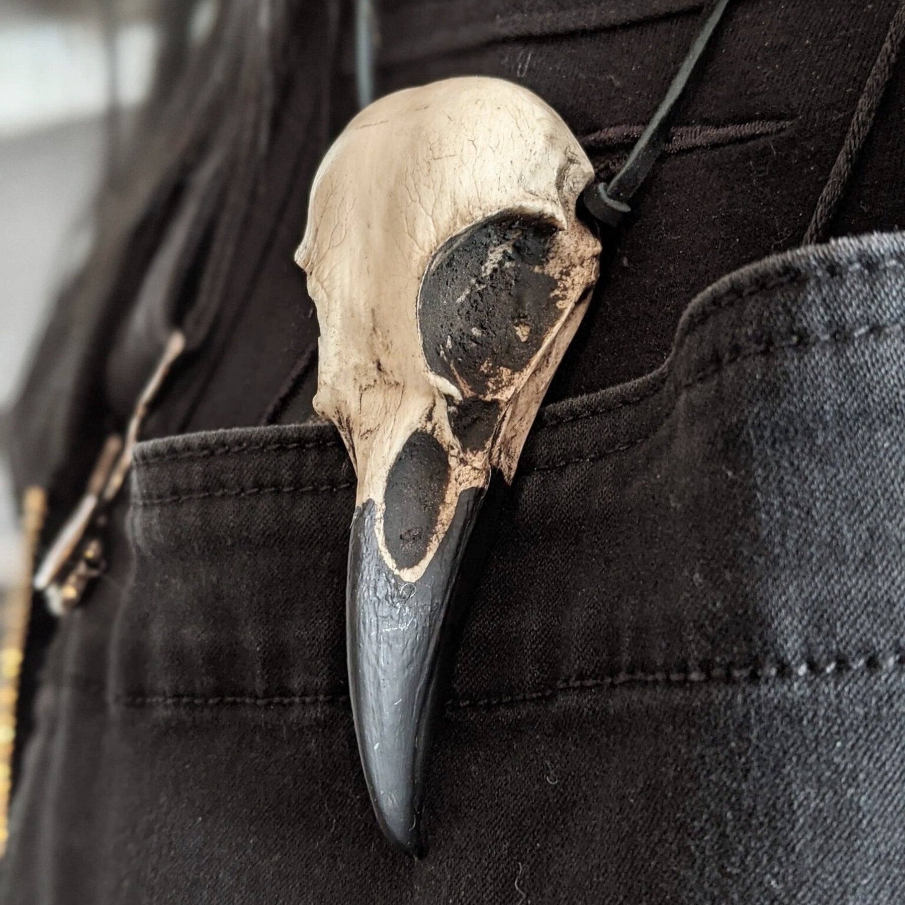 A life size resin raven skull necklace handmade by a skull jewelry artist and worn by gothic alt model. The style of the necklace is alternative and witchy for gothic fashion or Halloween. The bone jewelry pendant is brown with a black beak and looks like a real animal skull.