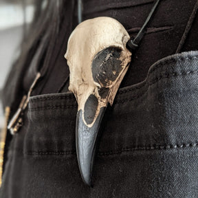 A life size resin raven skull necklace handmade by a skull jewelry artist and worn by gothic alt model. The style of the necklace is alternative and witchy for gothic fashion or Halloween. The bone jewelry pendant is brown with a black beak and looks like a real animal skull.