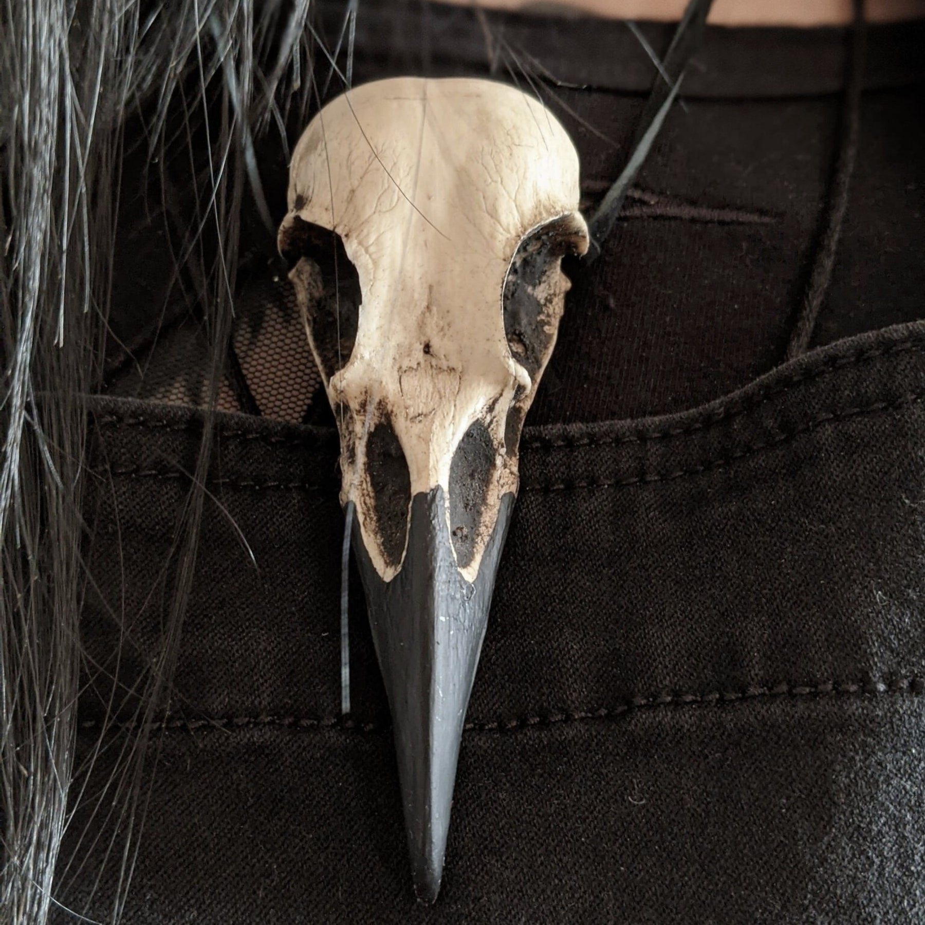A life size resin raven skull necklace handmade by a skull jewelry artist and worn by gothic alt model. The style of the necklace is alternative and witchy for gothic fashion or Halloween. The bone jewelry pendant is brown with a black beak and looks like a real animal skull.