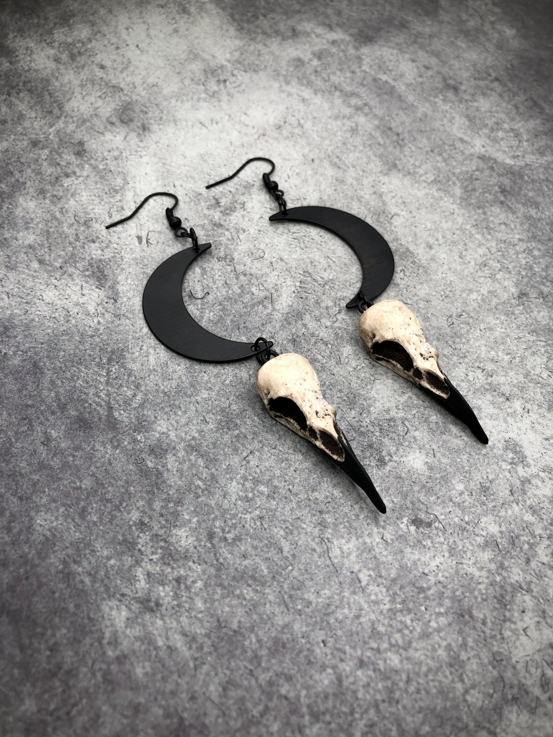 Side view of Dangle earlobe raven goth skull charm earrings with crescent moons and resin bird skulls.