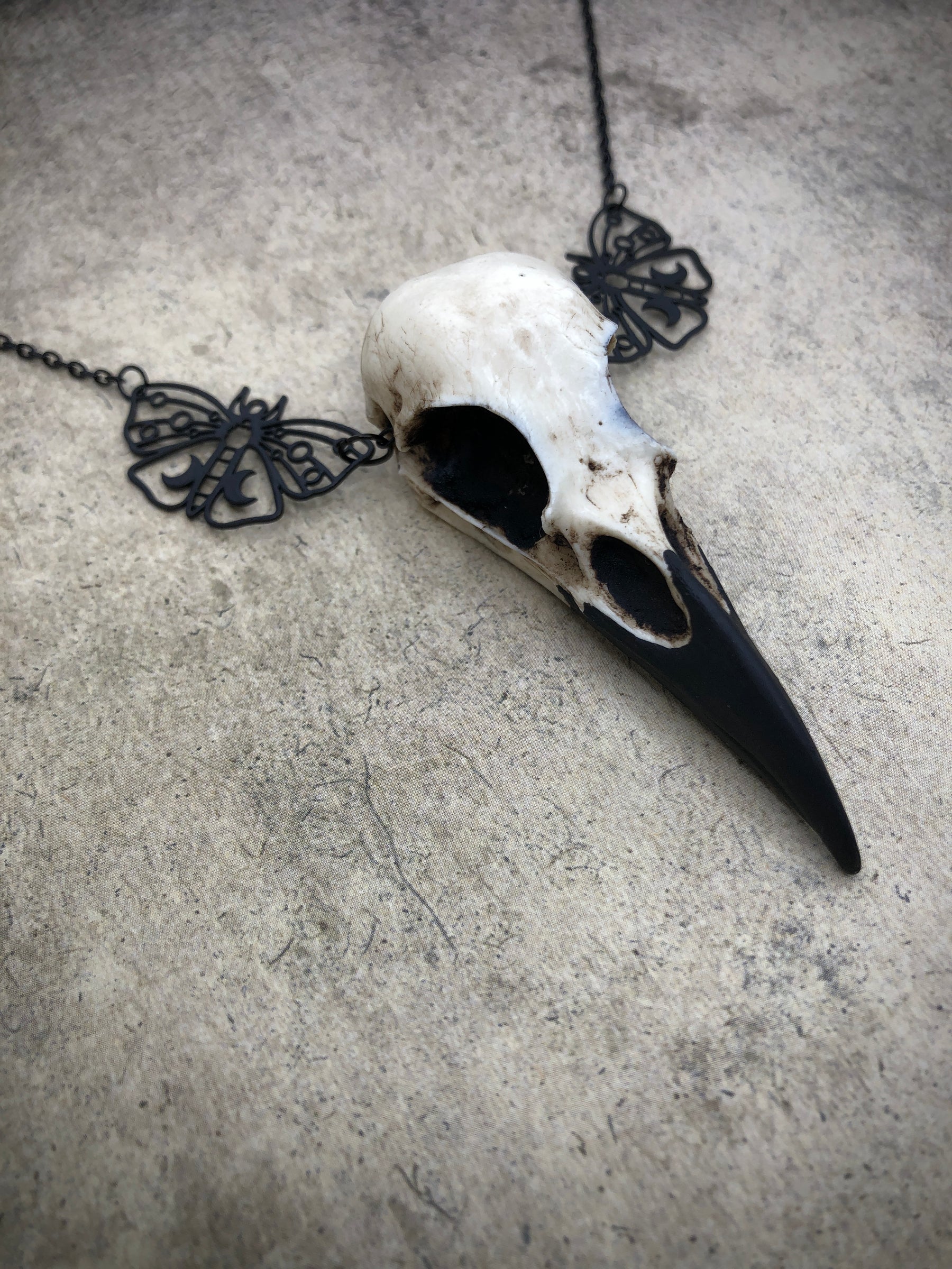 Side view of bone jewelry luna moth raven skull necklace featuring black crescent moon moth charms and a realistic resin bird skull.