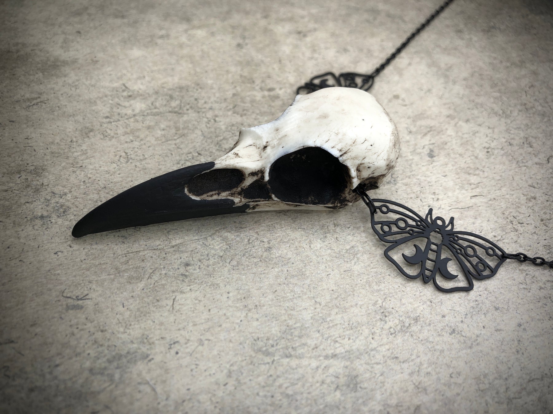 Left view of bone jewelry luna moth raven skull necklace featuring black crescent moon moth charms and a realistic resin bird skull.