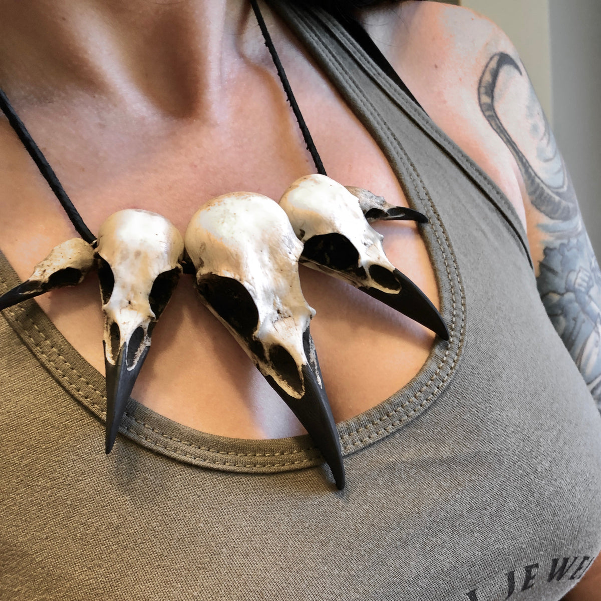 Bone collector bird skull raven skull necklace pendant worn by bone jewelry gothic model with tattoos. The necklace features five skulls.