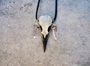 Close up of healing quartz crystal bird skull necklace raven pendant on suede leather cord and two crystal points.