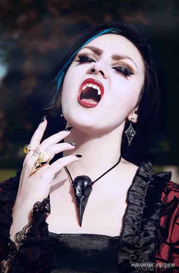 Vampire woman wearing Halloween raven skull necklace pendant with a black suede cord and a witchy gothic statement bird skull ring on her hand.